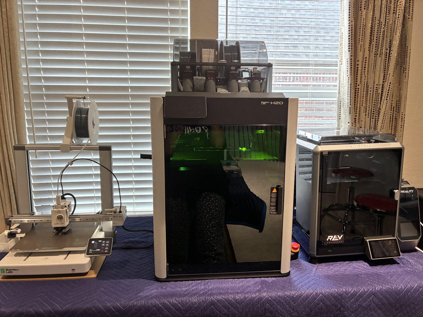 The print farm: Bambu Lab A1, Bambu Lab H2D with AMS on top, and Creality K1C side by side